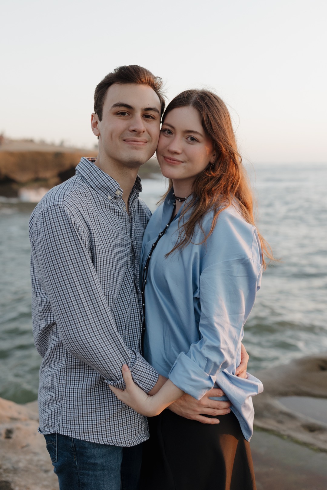 Katiuska y Daniel abrazados frente al mar, sonriendo a la cámara